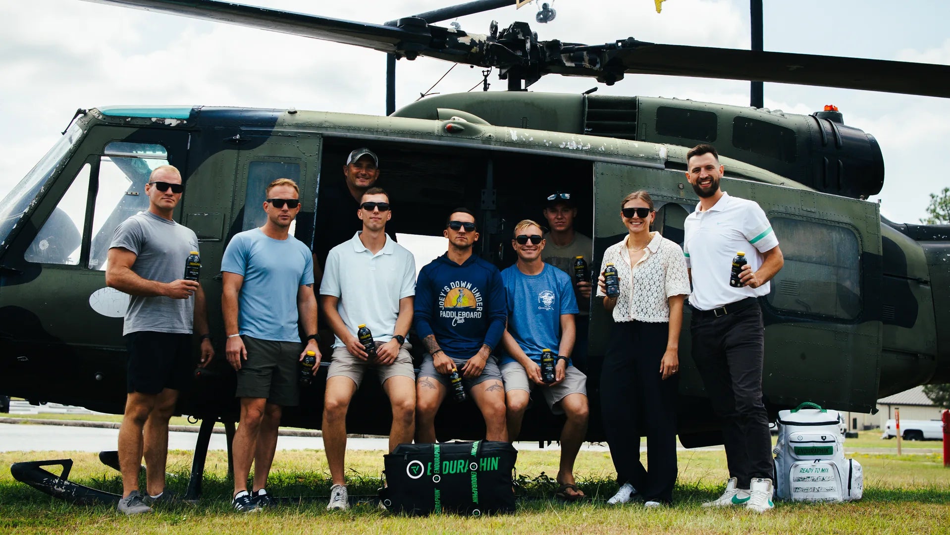 Enduraphin team and service members holding recovery bottles beside a military helicopter