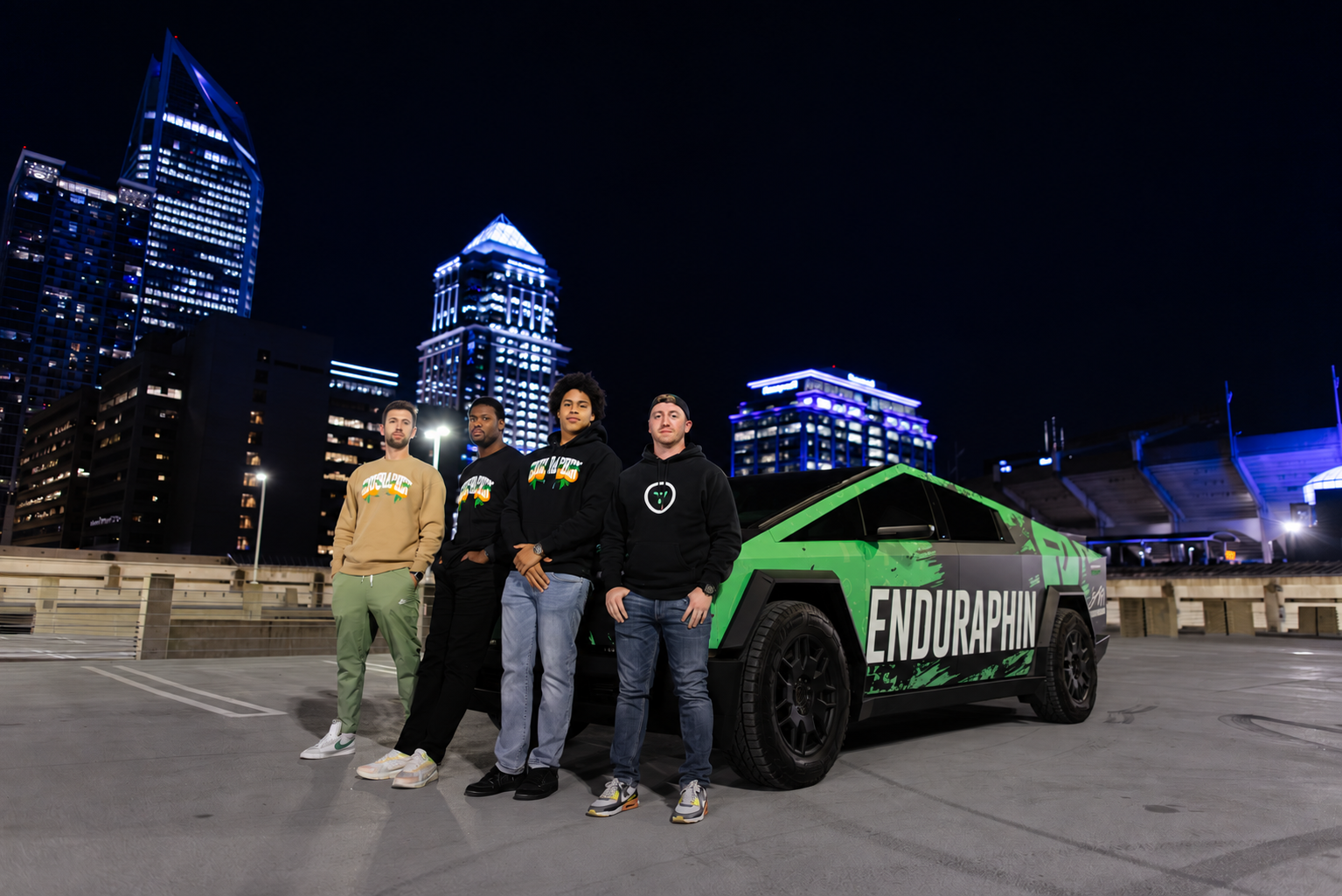 The Enduraphin community beside the branded green truck under a city skyline at night